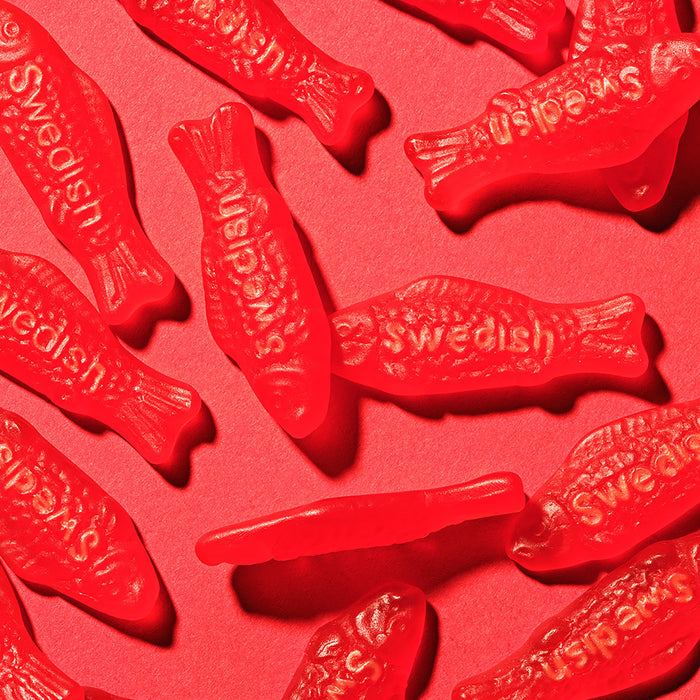 Red Swedish Fish gummy candies on a pink background