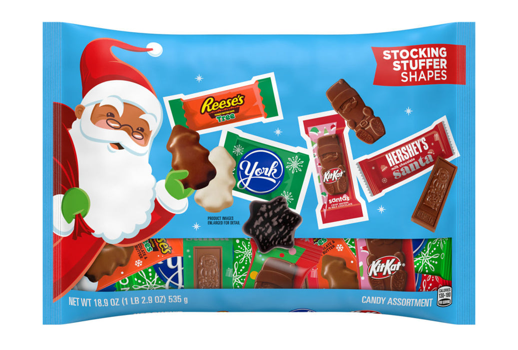 A festive blue candy assortment bag featuring Santa Claus on the left and several branded candy bars including Reese's, Yuck, Hershey's, and KitKat. The packaging includes the text 'STOCKING STUFFER SHAPES' and shows multiple colorful candy bars through a clear window.