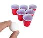 Red plastic cups with white lids arranged in a circle, with a hand holding a white ball above them.