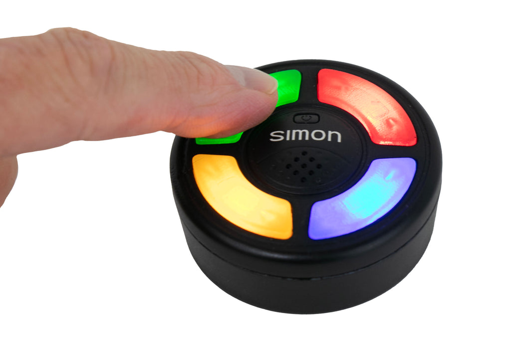 Hand pressing a Simon electronic game component with colored lights on a white background