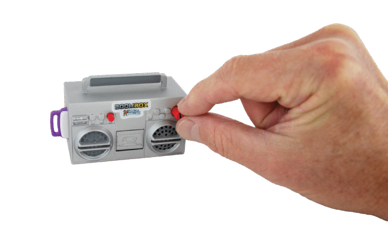 Hand holding a small gray toy boombox against a beige background