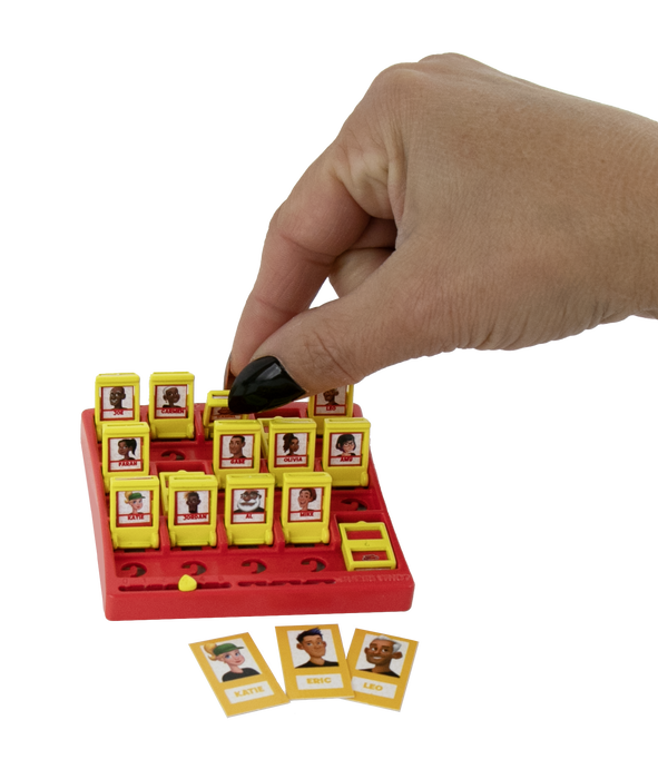 A hand with black nail polish is placing a small yellow card into a red and yellow board game. The board features multiple yellow slots containing cards with illustrated faces, and three separate character cards are displayed in front on a clean white background.