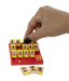 A hand with black nail polish is placing a small yellow card into a red and yellow board game. The board features multiple yellow slots containing cards with illustrated faces, and three separate character cards are displayed in front on a clean white background.