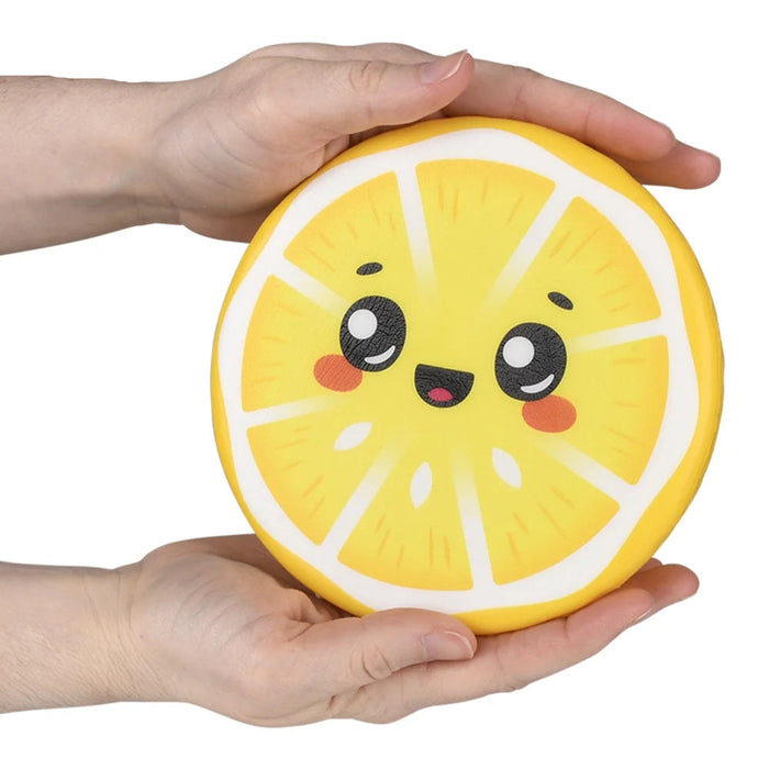 A person's hands holding a round, yellow lemon-slice-shaped squishy toy with a cute cartoon face, set against a plain white background.