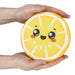 A person's hands holding a round, yellow lemon-slice-shaped squishy toy with a cute cartoon face, set against a plain white background.
