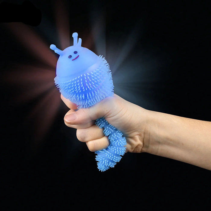 A hand holding a light blue squishy, spiky novelty toy against a black background with a glow effect. The logo 'Brain Kind Novelty' is visible in the top-left corner.
