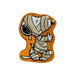 A metal candy filled tin featuring Snoopy mummy figure patch or applique on a white background. Snoopy is wrapped in beige bandages with black outlines, set against an orange shape background.