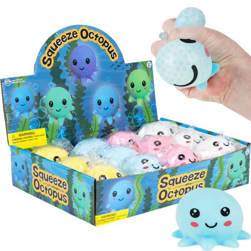 A retail display box filled with small squishy octopus toys, with a hand holding one light blue octopus above the box. The display packaging is blue with cartoon octopus graphics and the words 'Squeeze Octopus.